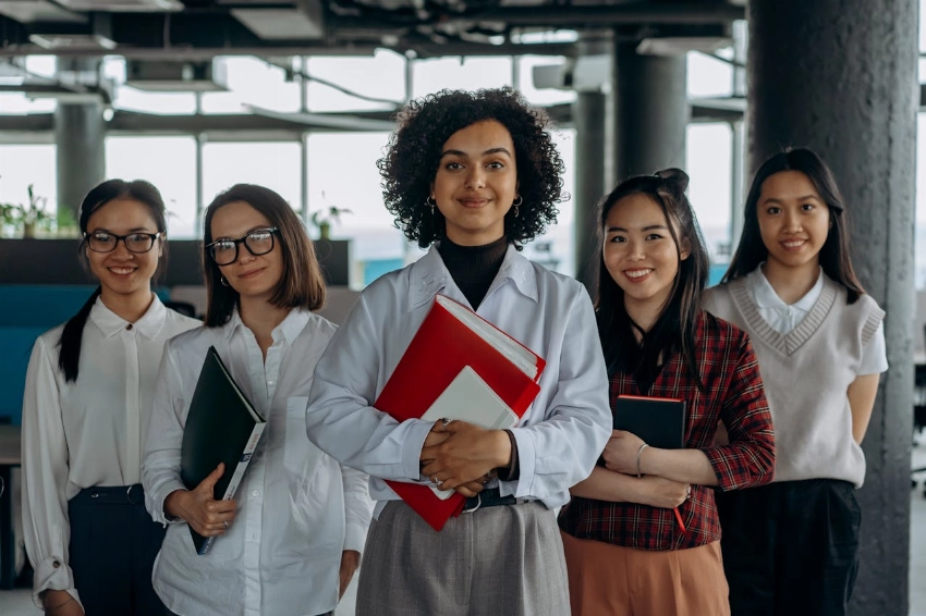 Group of diverse women colleagues smiling in a modern office setting, holding documents