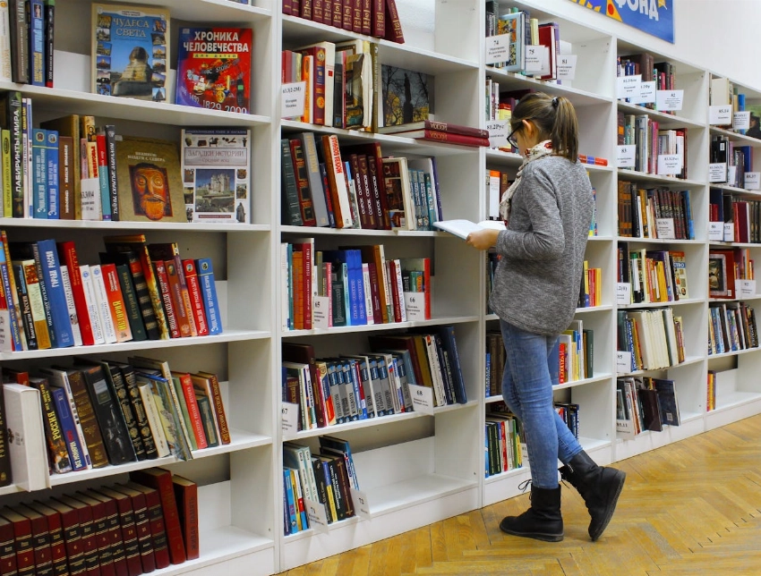 A young woman stands reading a book in a well-stocked library