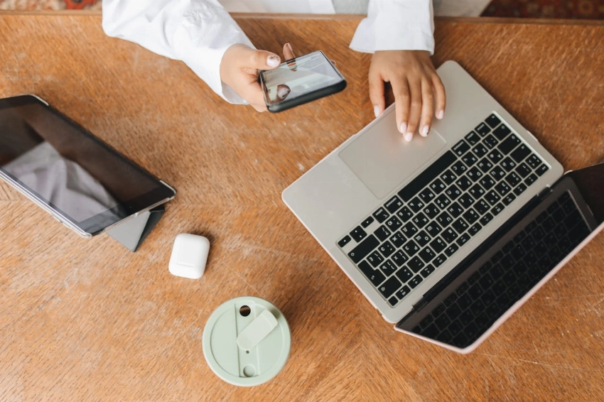 Top view of a workspace featuring a laptop, tablet, phone, and beverage. Perfect for remote work context