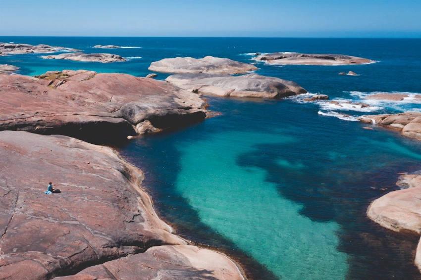 Clean blue water of tranquil water of ocean surrounded with stony terrain under cloudless blue sky