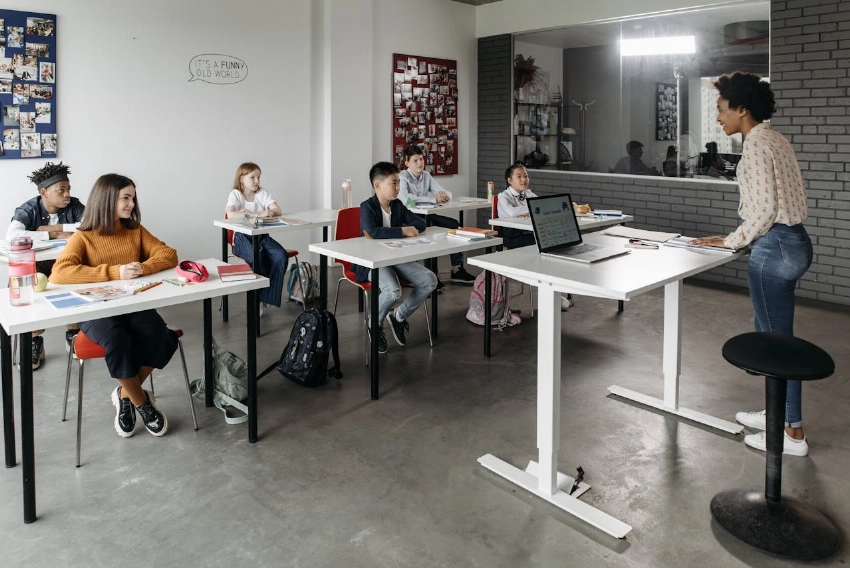 A diverse group of students attentively listens to a teacher in a modern classroom setting