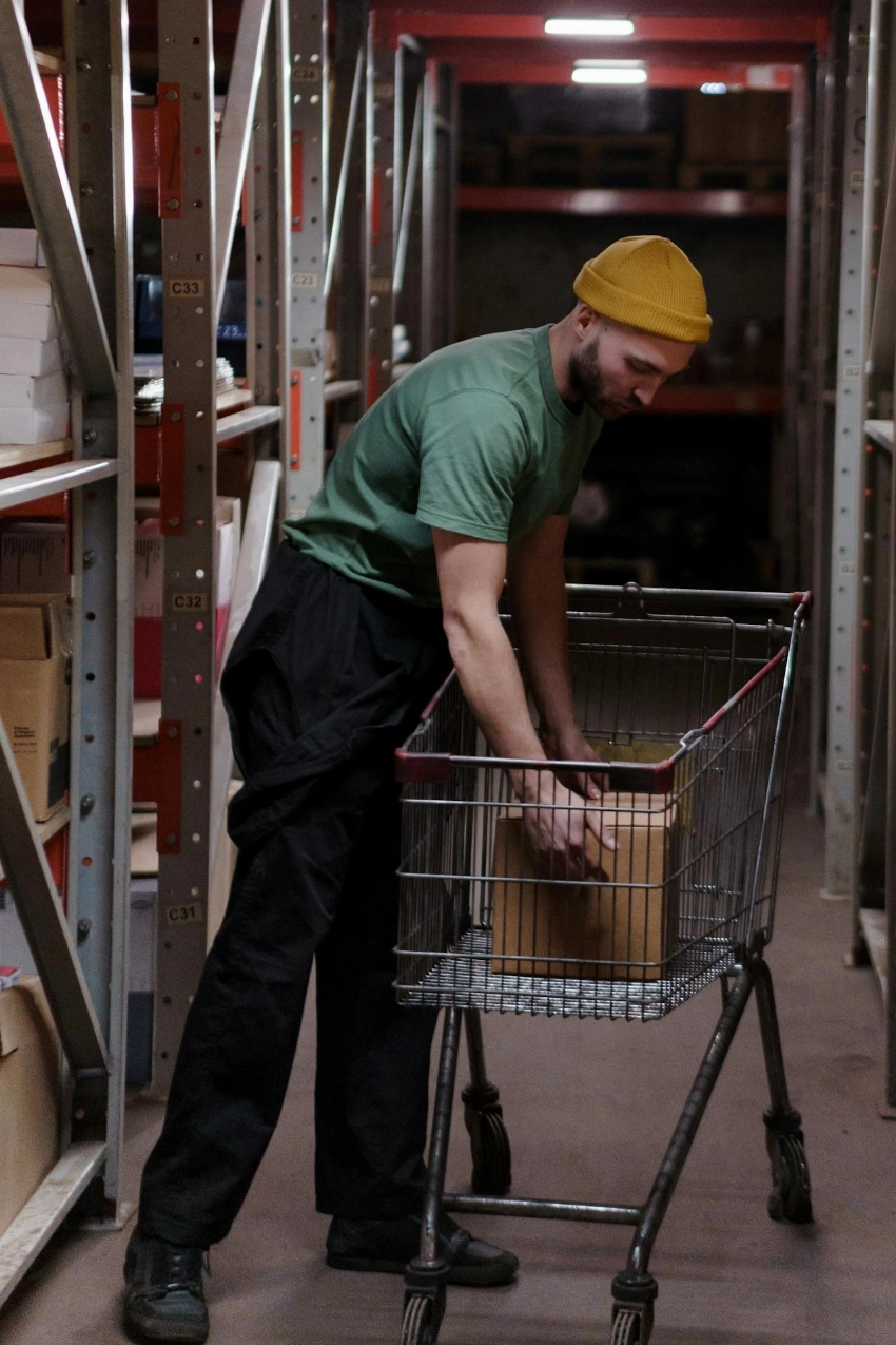 A man in a green shirt and hat organizes boxes in a warehouse, showcasing efficient storage work